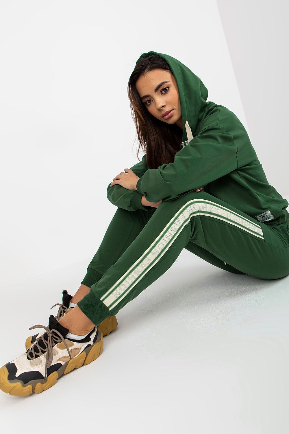 Sophisticated model in a deep green cotton-blend hoodie and pants set, seated gracefully, displaying the comfort and style of the outfit.