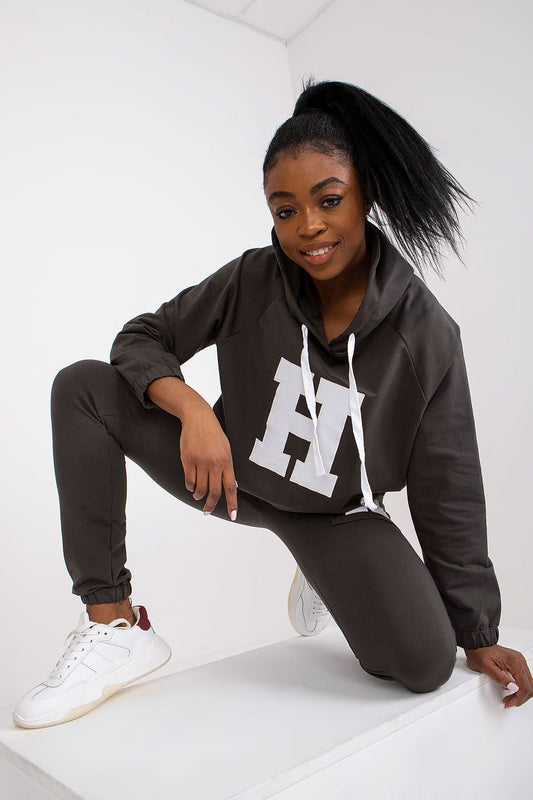 Stylish woman in luxury dark grey hoodie and pants set, featuring a prominent logo, showcasing a sleek modern look combined with comfort.