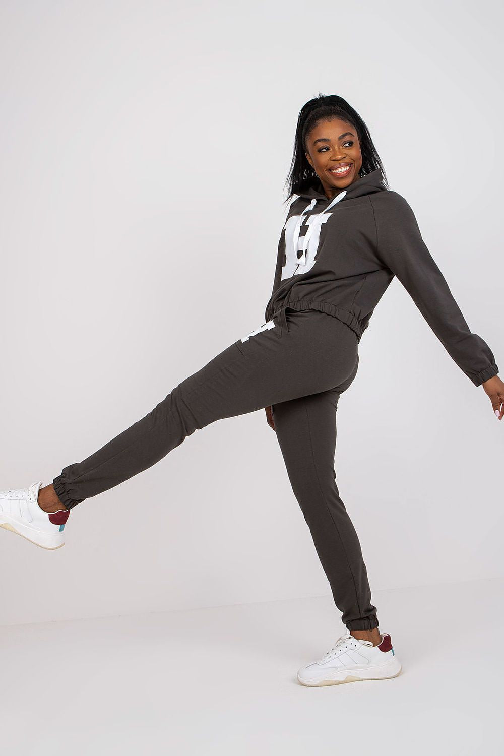 Chic model elegantly posing in dark grey luxury hoodie and pants set, highlighting comfort and fashion with stylish sneakers.