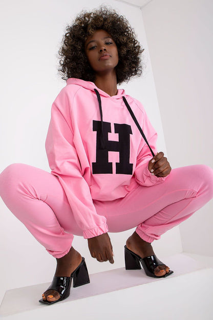 Glamorous model crouching in a vibrant pink luxury hoodie and pants ensemble, highlighting trendy fashion paired with chic footwear.