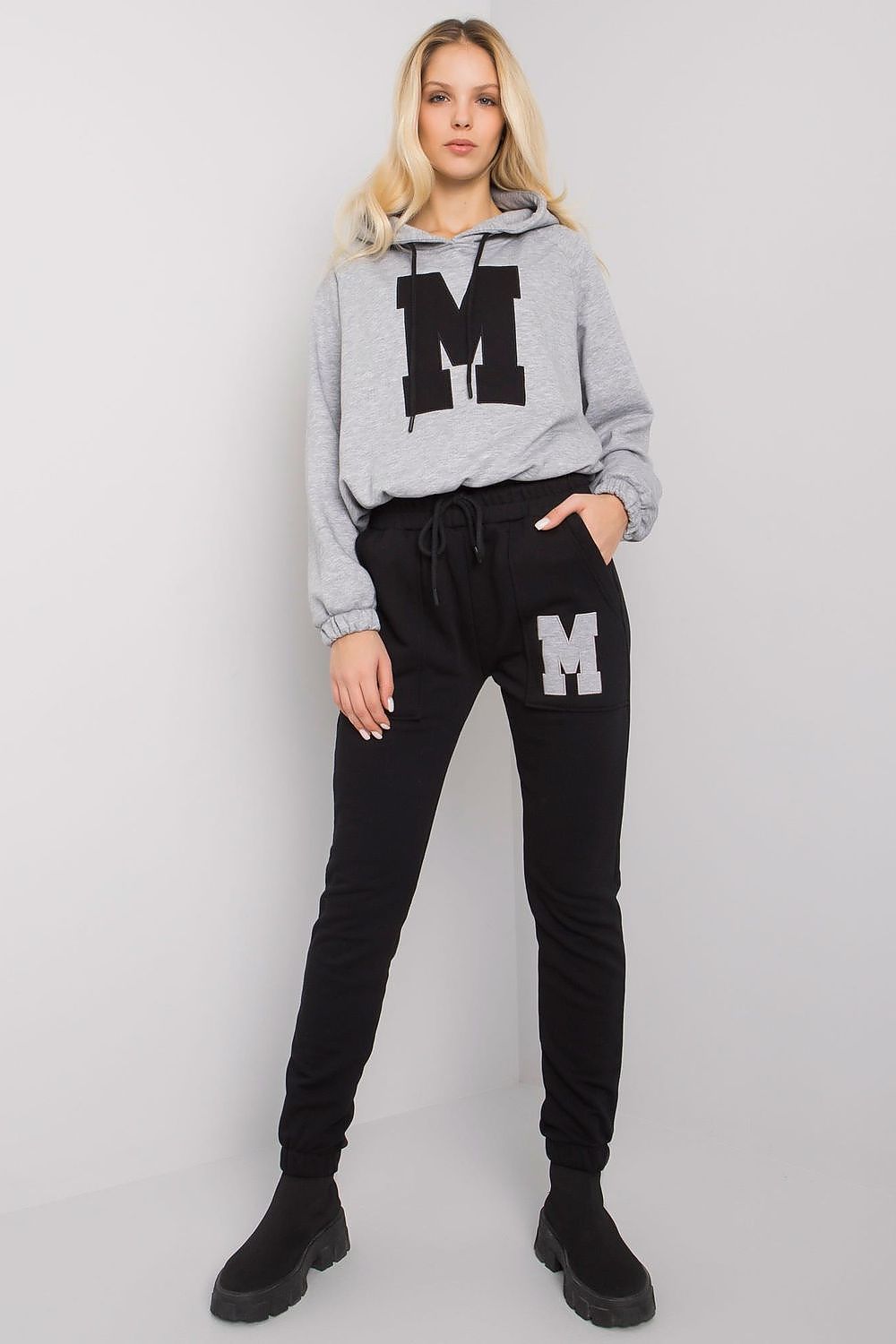 Elegant women's loungewear set featuring a grey hooded sweatshirt with a prominent letter 'M' print, paired with stylish black tapered pants, perfect for both comfort and chic style.