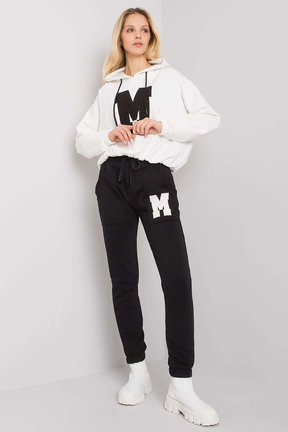 Stylish women's loungewear comprising an ivory hoodie with a black letter 'M' design, accompanied by elegant black tapered pants, perfect for luxury casual styling.