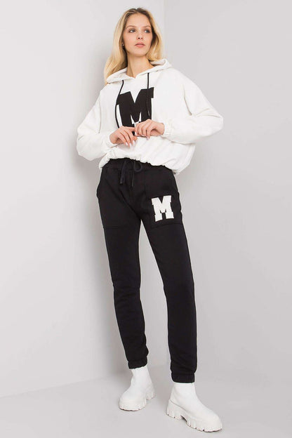 Stylish women's loungewear comprising an ivory hoodie with a black letter 'M' design, accompanied by elegant black tapered pants, perfect for luxury casual styling.