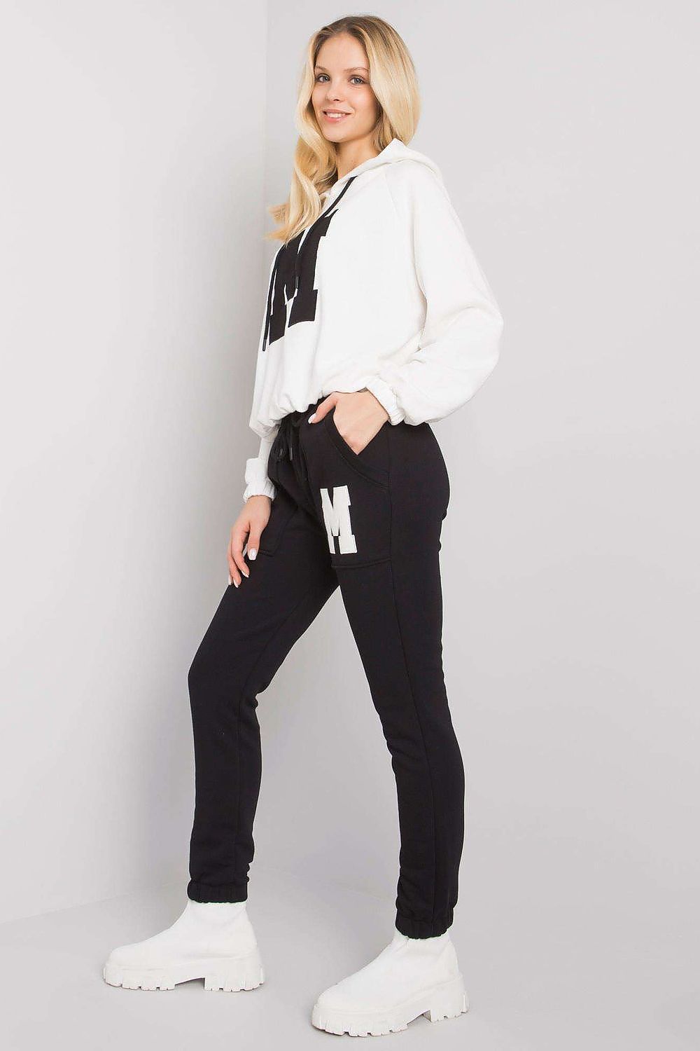 Refined look at a women's loungewear ensemble featuring a white hoodie with a letter 'M', matched with chic black trousers, embodying a blend of comfort and luxury.
