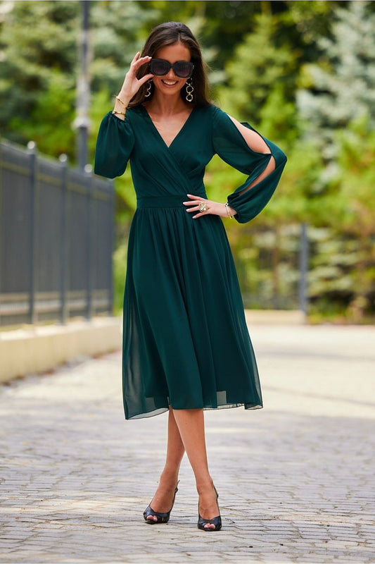 Elegant green midi cocktail dress featuring long buff sleeves and an exposed back, styled for a chic outdoor setting. Perfect for formal events.