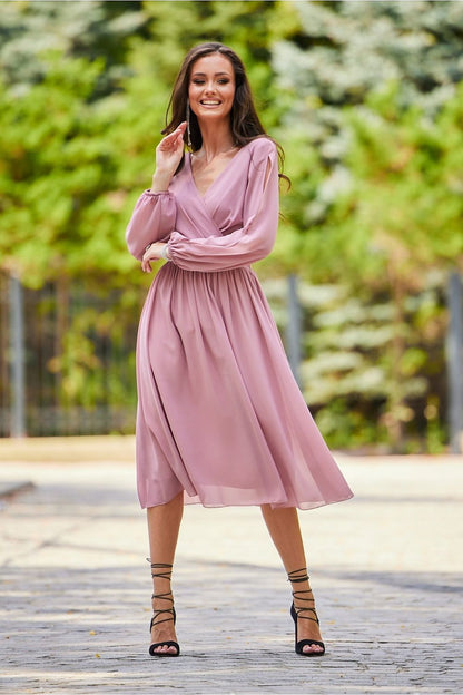 Graceful pink midi cocktail dress with long buff sleeves and a flattering wrap design, showcased in a sophisticated outdoor environment, perfect for weddings.