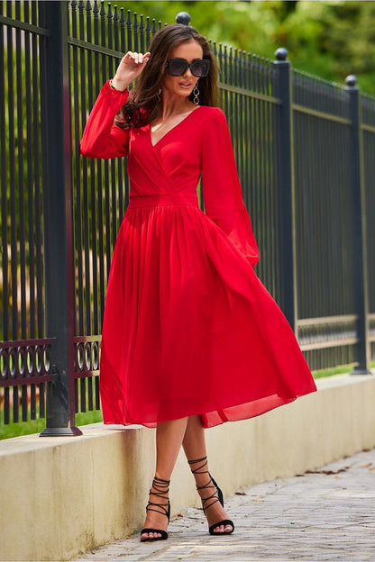 An enchanting model in a luxurious red midi cocktail dress with long sleeves and an exposed back, exuding sophistication and elegance. The dress features a wrap style complemented by delicate ankle strap heels.