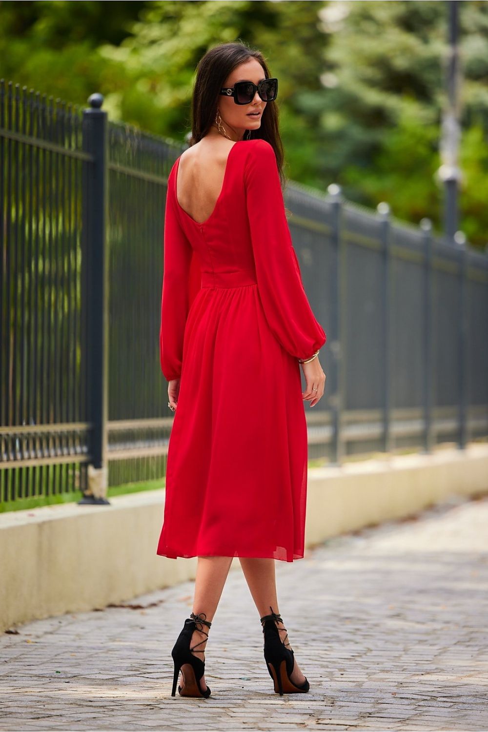A stunning rear view of a model in a glamorous red midi dress with long buff sleeves and an alluring exposed back, radiating classy sophistication with stylish strappy heels, perfect for upscale events.