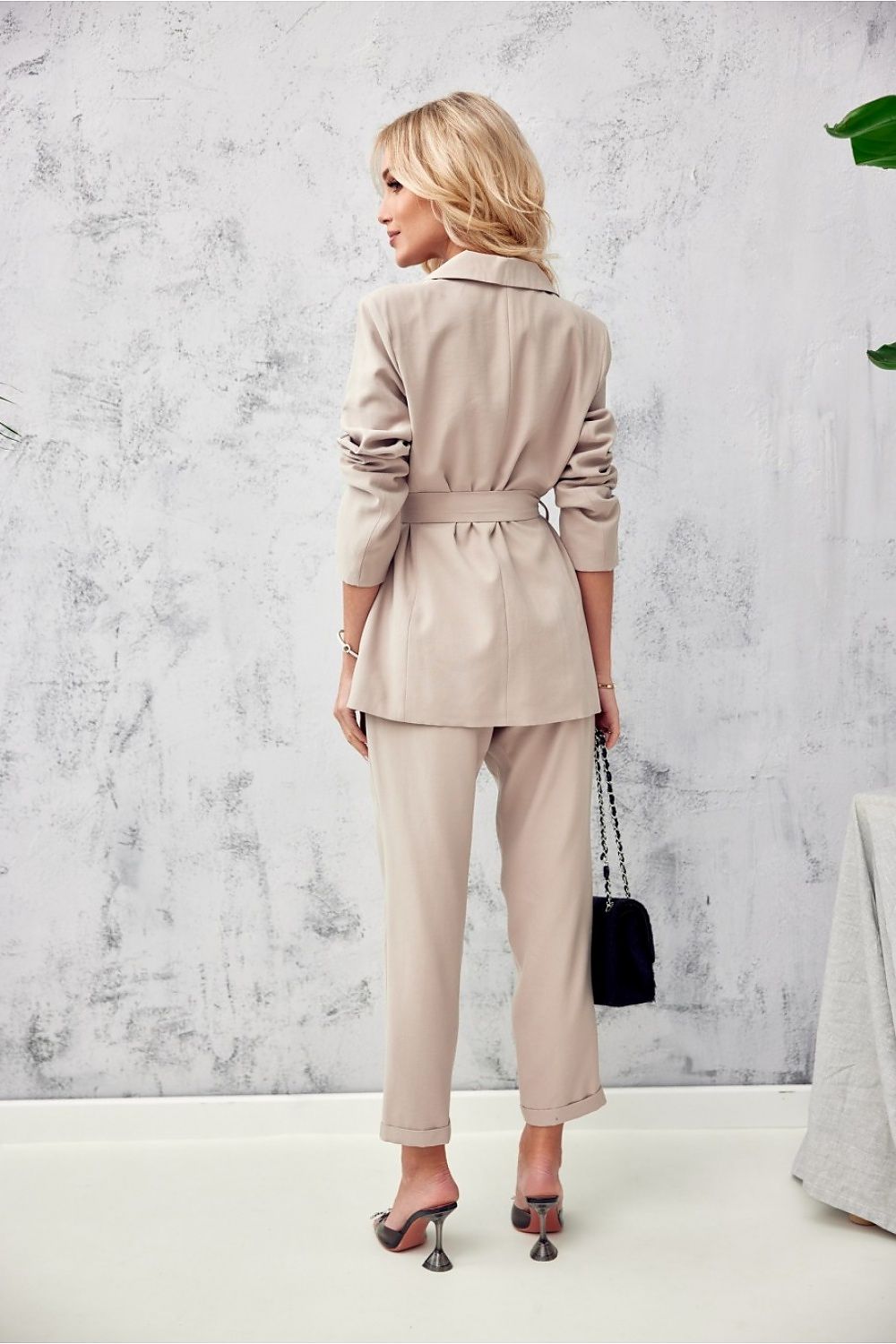 Graceful view of a blonde model in a sophisticated beige suit by Roco Fashion, captured from the back, demonstrating the outfit's elegant fit and detailing amidst a modern decor.