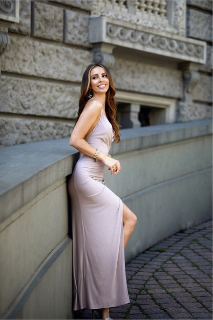 Elegant long evening dress featuring an open back and glitter accents, model posing on a stone wall in a sophisticated outdoor setting.