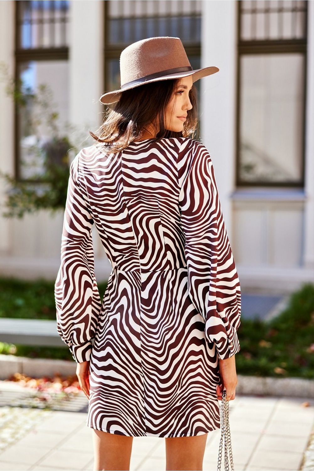 Back view of a chic zebra print mini dress with long puff sleeves, worn by a model with a hat in a charming outdoor setting, ideal for various celebrations.