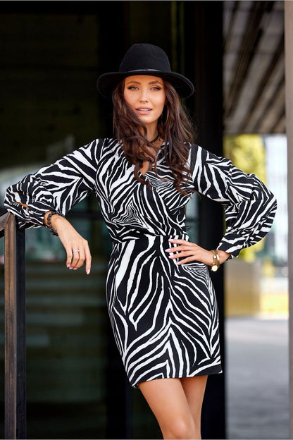 Sophisticated black and white zebra print mini dress with a deep neckline, modeled by a woman alongside modern architecture, exuding elegance and style for special events.