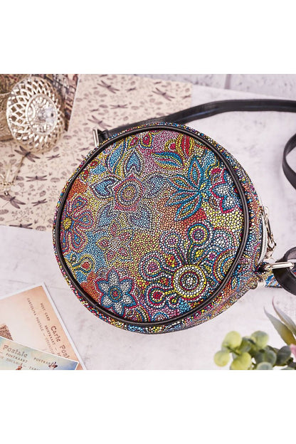 Stylish round handbag viewed from above, featuring an intricate floral motif in lively colours against a black leather background, ideal for adding a touch of luxury to any outfit.