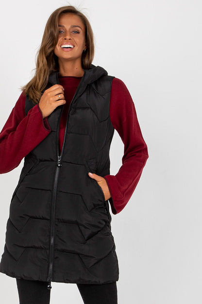 A stylish woman wearing a luxury NM gilet in black, made of 100% polyester. The vest features a zip front and hood, complementing her elegant outfit.