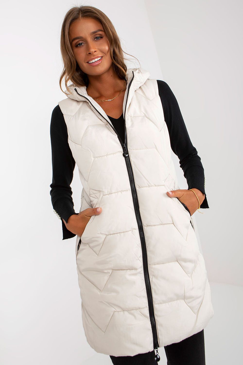Elegant model showcasing a luxury NM gilet vest in soft cream colour, featuring a zip front and hood, styled over a black top, exuding sophistication.