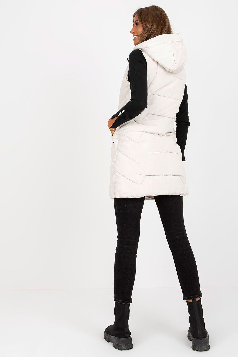 Back view of a fashionable model wearing a cream hooded NM gilet vest over black jeans, highlighting the modern cut and luxurious fabric for a contemporary look.