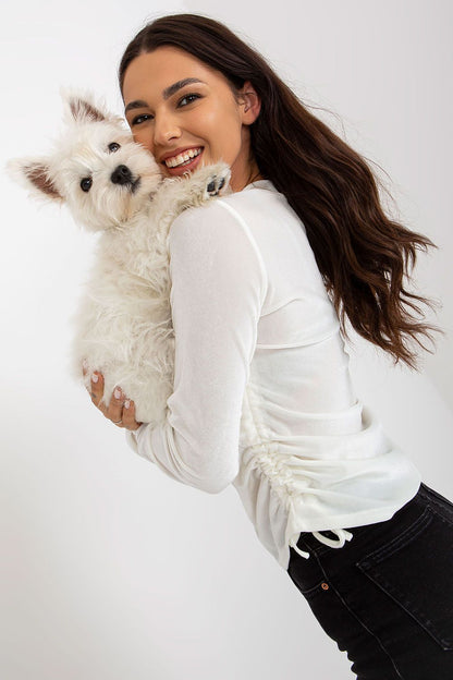 Charming model smiling while holding a fluffy white dog, wearing a white luxurious velour blouse with long sleeves and side ties, exuding warmth and elegance.