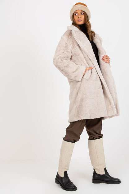 Sophisticated beige fur coat by Och Bella, displayed in a modern pose with matching brown trousers and a warm hat, exuding luxury and comfort for winter wear.