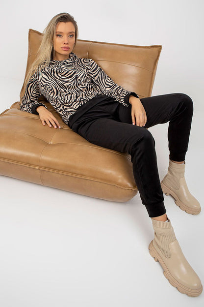 Model reclining on a chic leather couch, elegantly dressed in the Rue Paris velour outfit with animal print details, exuding sophistication and style.