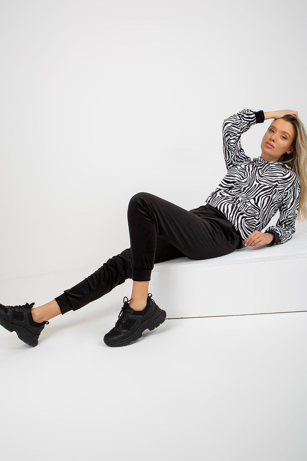 Model lounging in the stylish Rue Paris velour set with animal print sweatshirt and black pants, presenting a relaxed yet chic appearance with sporty footwear.