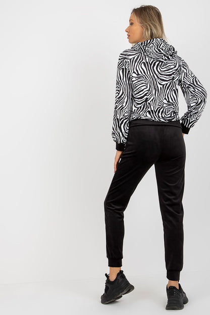 Elegant woman showcasing the luxurious Rue Paris velour set featuring a stylish animal print sweatshirt with a hood and chic black long pants, perfectly rounded off with sporty black sneakers.