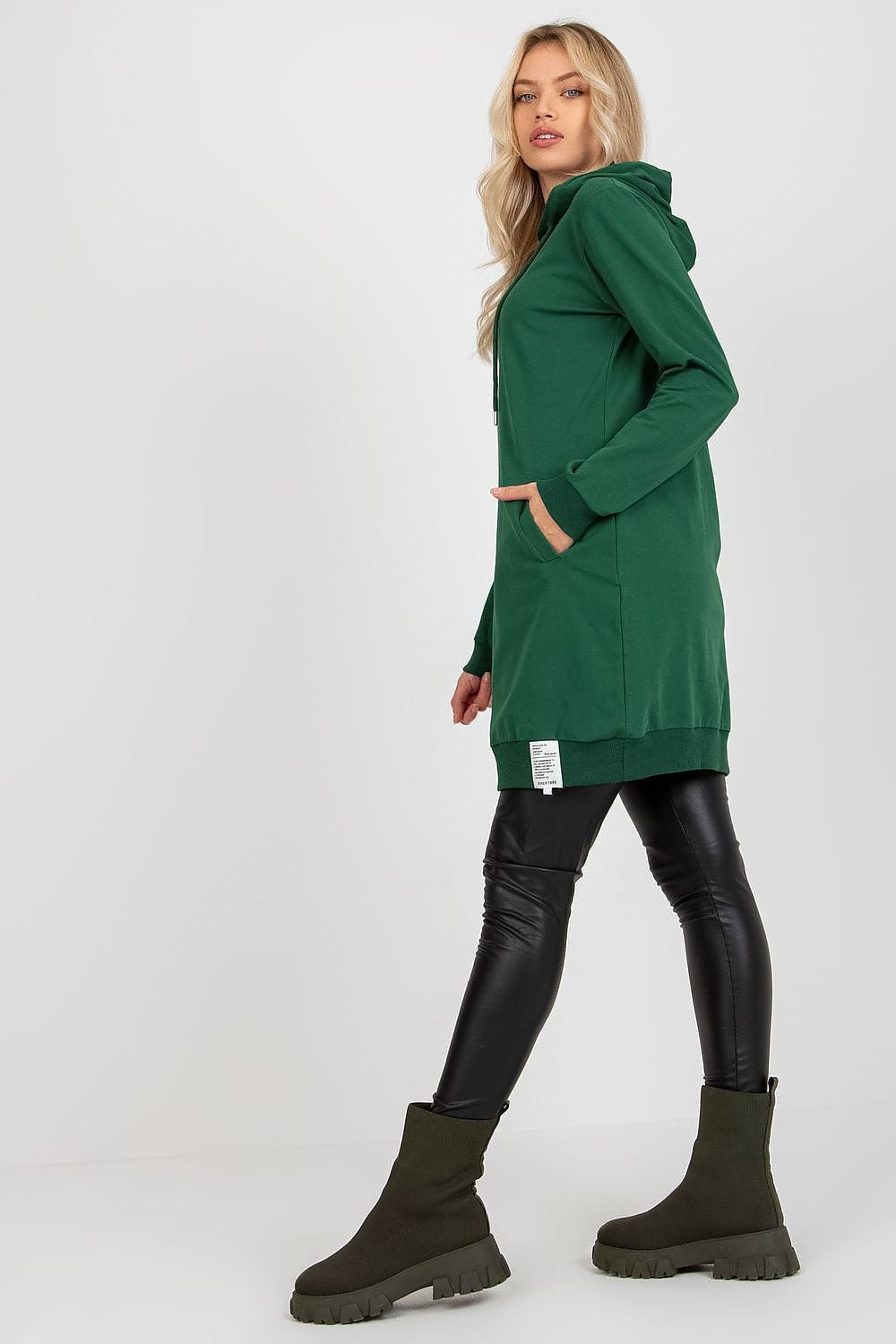 Sophisticated image of a model showcasing a green women's sweat dress with a hood and pockets, accentuated by black leggings and fashionable ankle boots, offering a luxurious comfort look.