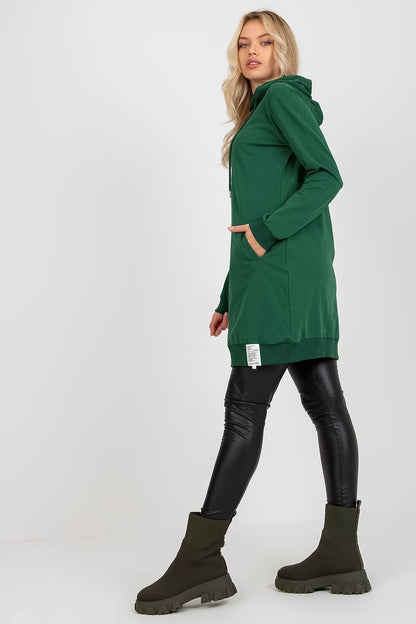 Sophisticated image of a model showcasing a green women's sweat dress with a hood and pockets, accentuated by black leggings and fashionable ankle boots, offering a luxurious comfort look.