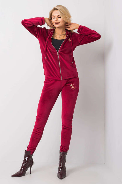 Chic model wearing a vibrant burgundy velour two-piece set featuring a zip-up hooded sweatshirt and tailored pants, highlighted by fashionable ankle boots.