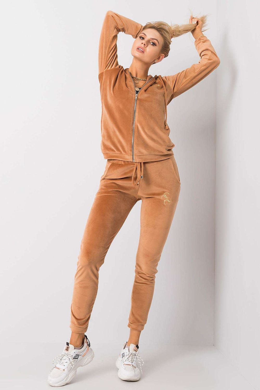 Fashion-forward model flaunting a contemporary tan velour two-piece ensemble, featuring a zippered hooded sweatshirt and elegant trousers, styled with trendy sneakers.