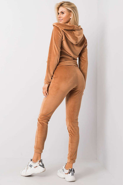 Elegant woman showcasing a luxurious velour 2-piece set featuring a hooded sweatshirt with a zipper and matching pants with a tie waist, perfect for chic casual wear. The set is styled in a warm, rich colour, complemented by trendy white sneakers.