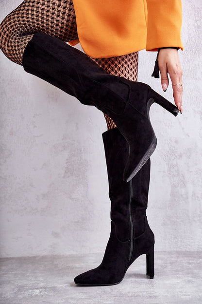 Elegant black eco-suede knee-high heel boots featuring a sleek design, side zip closure, and a pointed toe, styled with trendy fishnet tights and an orange blazer.