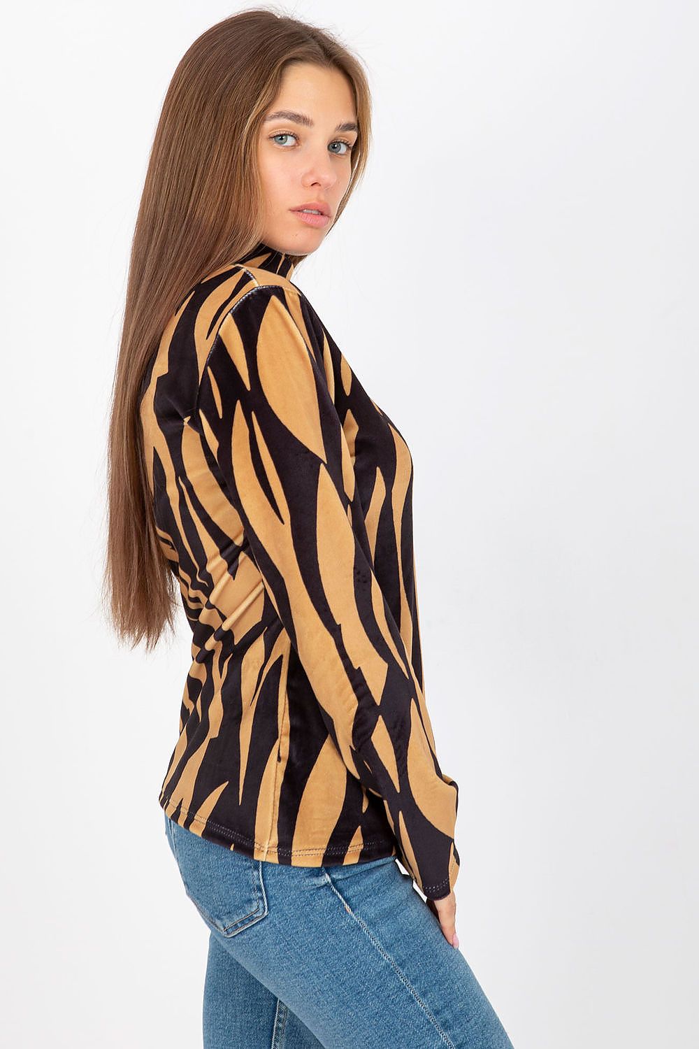 Side view of a woman wearing a luxury velour blouse with a stand-up collar and long sleeves, featuring a striking black and gold abstract pattern, styled with casual denim jeans.