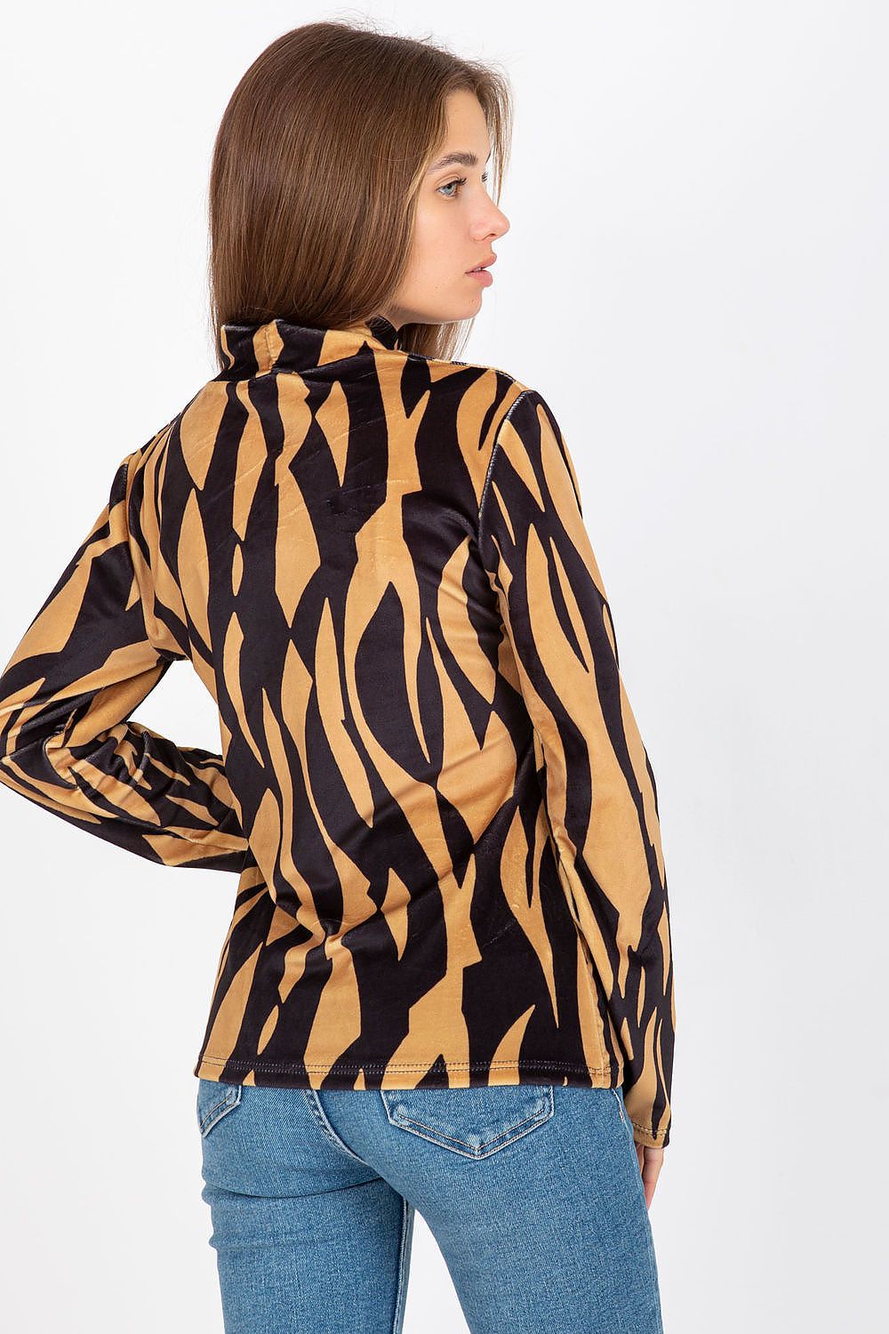 Back view of a woman dressed in an elegant luxury velour blouse with long sleeves and a stand-up collar, showcasing a bold black and gold design paired with form-fitting denim.
