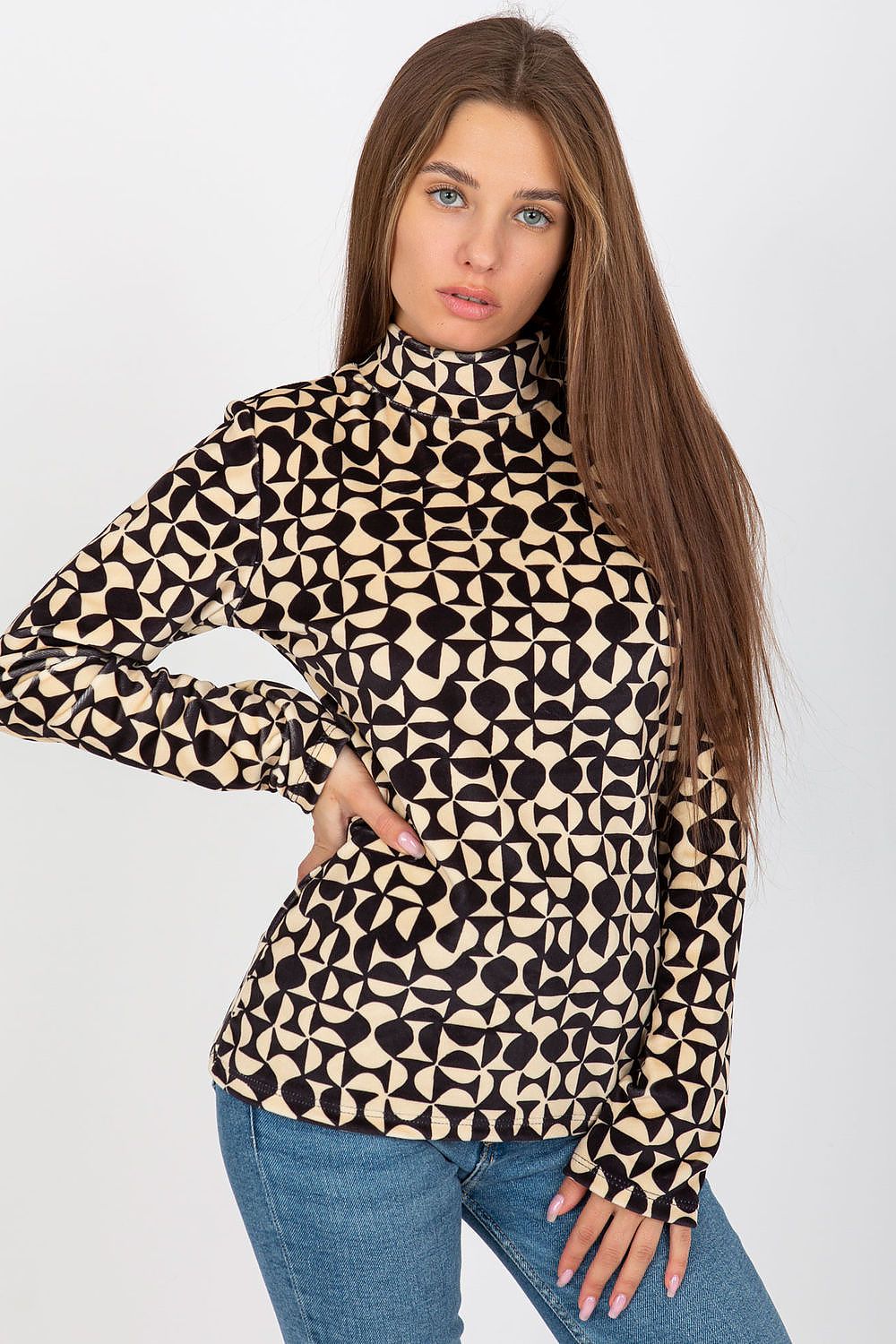 A woman in a chic luxury velour blouse with a stand-up collar and long sleeves, adorned with a distinctive beige and black geometric pattern, elegantly styled with fitted jeans.