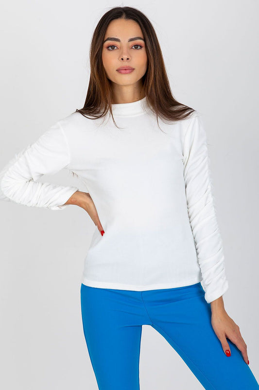 Stylish model showcasing an elegant white velour blouse with long sleeves and a stand-up collar, complemented by vibrant blue trousers, exuding sophistication and grace.