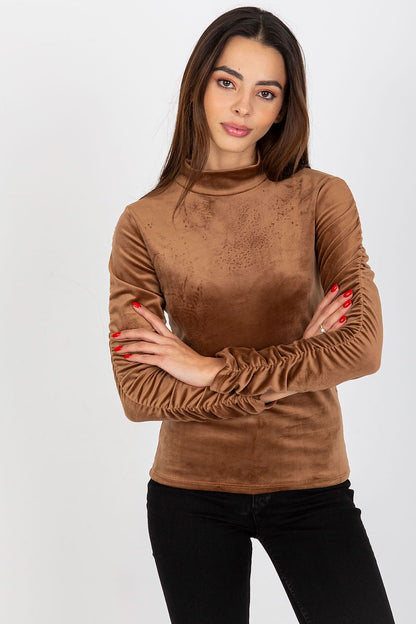 Luxurious brown velour blouse with long sleeves and gathering details on the sleeves, modelled by a woman with an elegant pose.