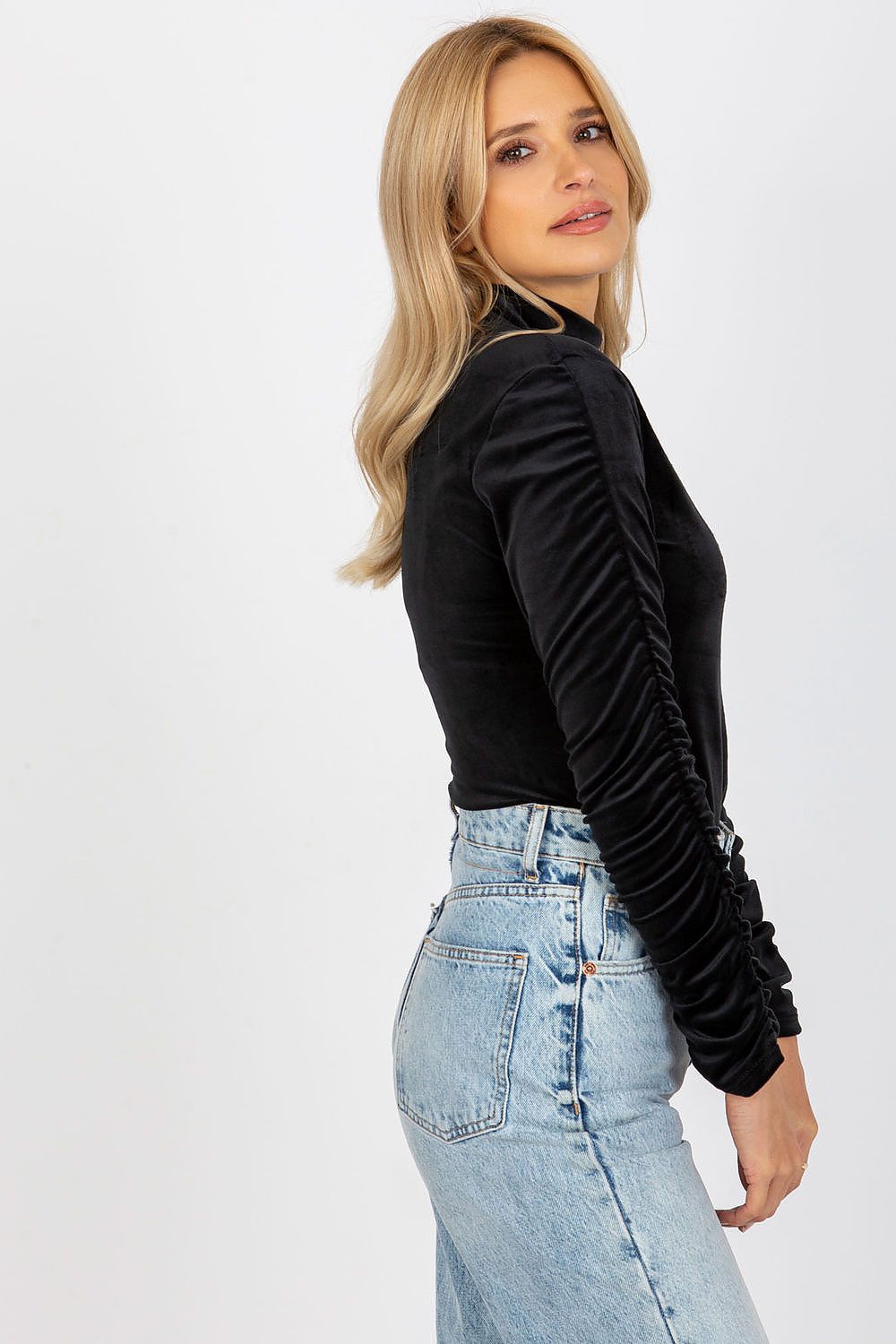 Side view of a luxurious black velour blouse showcasing long, beautifully gathered sleeves and a sophisticated stand-up collar, paired with vintage-style jeans.
