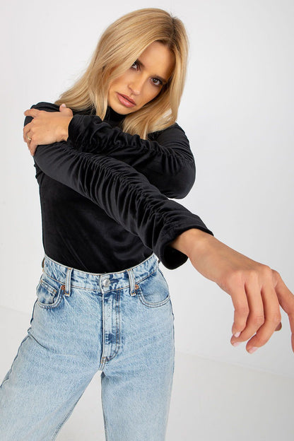 Close-up of a model wearing a black velour blouse with distinctive ruched sleeves and a flattering stand-up collar, emanating sophisticated elegance.