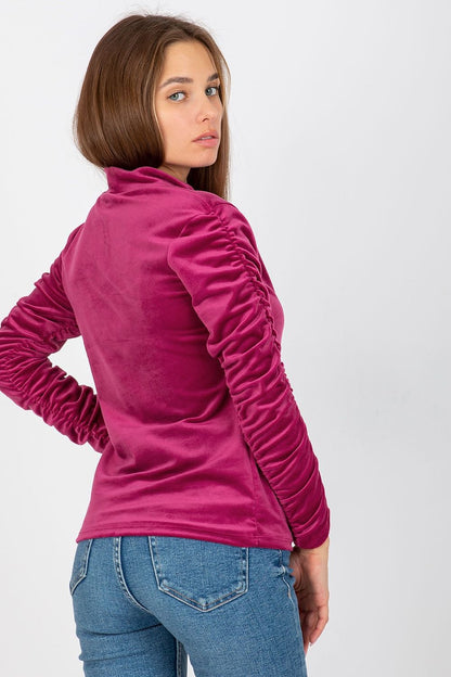 Back view of a luxurious pink velour blouse with long sleeves, showcasing detailed ruching, elegantly worn by a model.