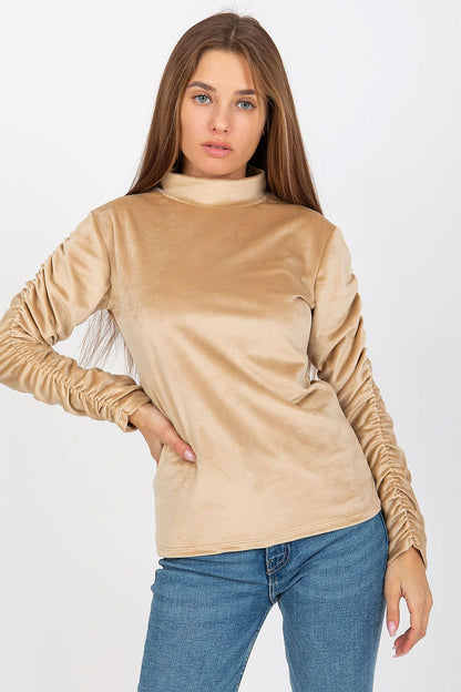 Sophisticated velour blouse in a soft beige tone, featuring long sleeves with decorative ruching, modeled to emphasize luxury and elegance.