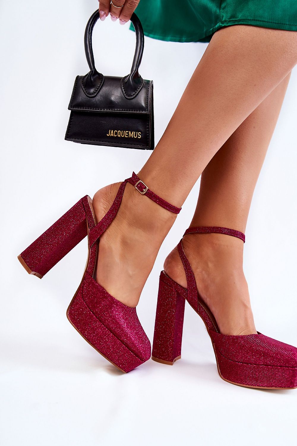 Trendy pink glittery platform stiletto sandals with buckle ankle strap, held by a fashionable woman alongside a chic black handbag. Perfect combination for a stylish night out.