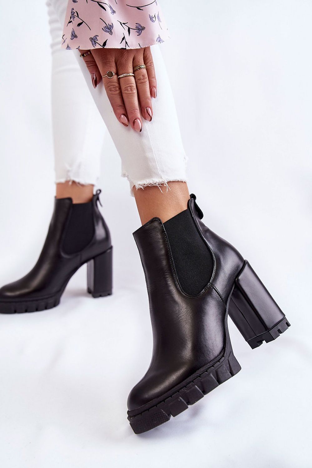 Close-up view of luxury women's trapper heel boots made from premium leather, showcasing the chic design with a striking platform, paired with fashionable white jeans and a pink floral top.