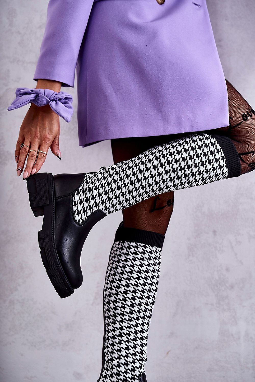 Stunning women's eco leather thigh-high boots with houndstooth knit, elegantly styled with a tailored purple blazer. Emphasizing the luxurious flat heel and contemporary fashion statement.
