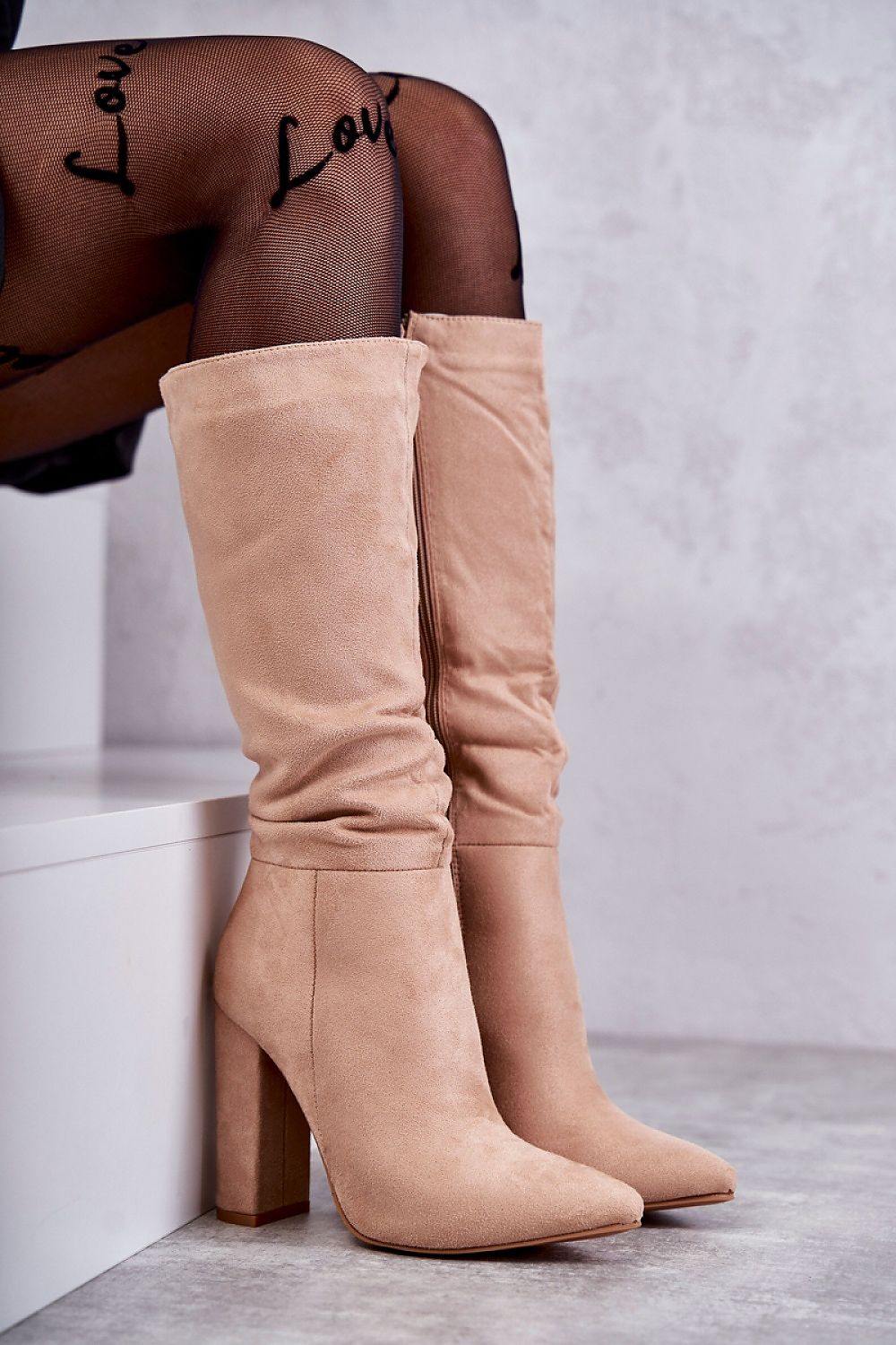 Elegant luxury pointed toe Cossack heel boots in soft beige suede, featuring a zippered front and warm insulation, styled elegantly with fishnet tights. Perfect for versatile fashion, ideal for both dresses and skirts.