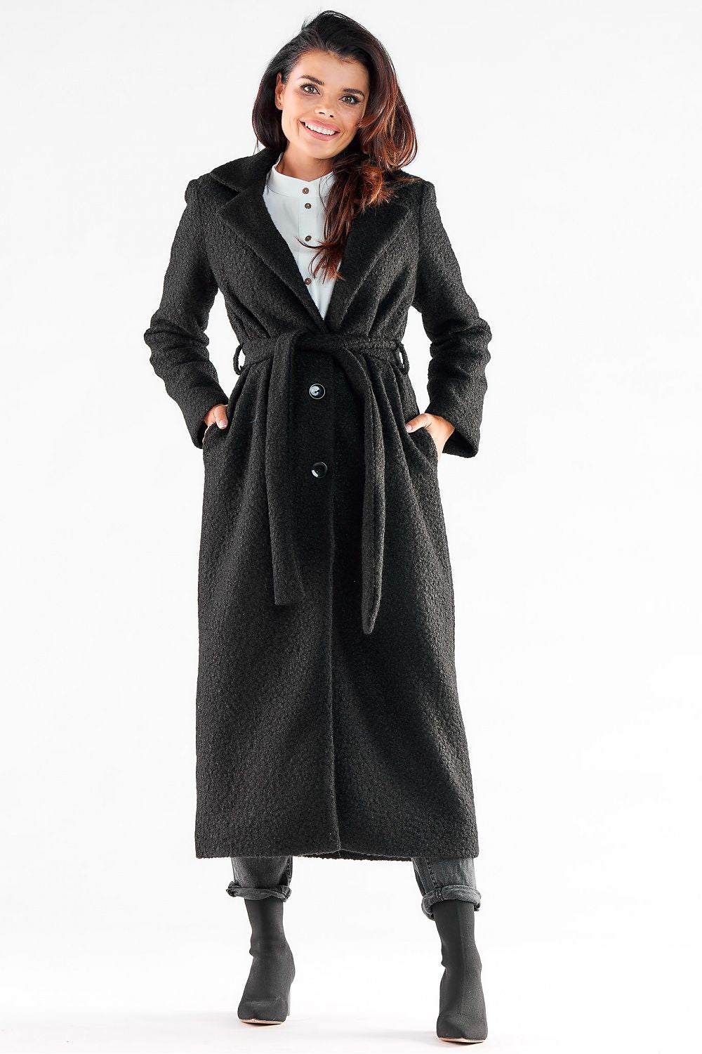 Stylish woman in an elegant black maxi coat by Awama, featuring a belted waist and three-button closure, perfect for sophisticated outings.