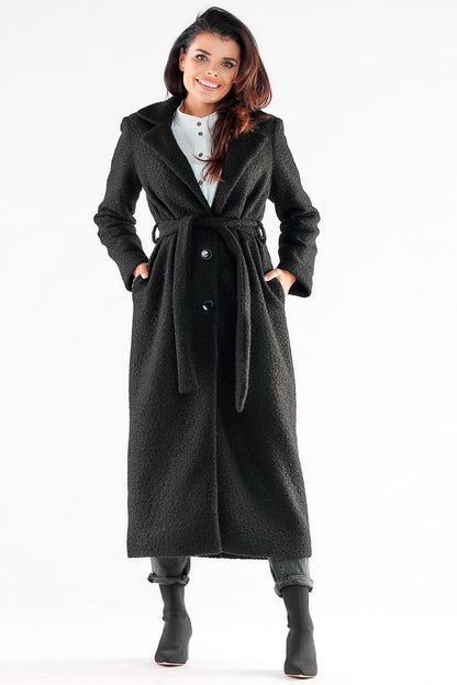 Stylish woman in an elegant black maxi coat by Awama, featuring a belted waist and three-button closure, perfect for sophisticated outings.