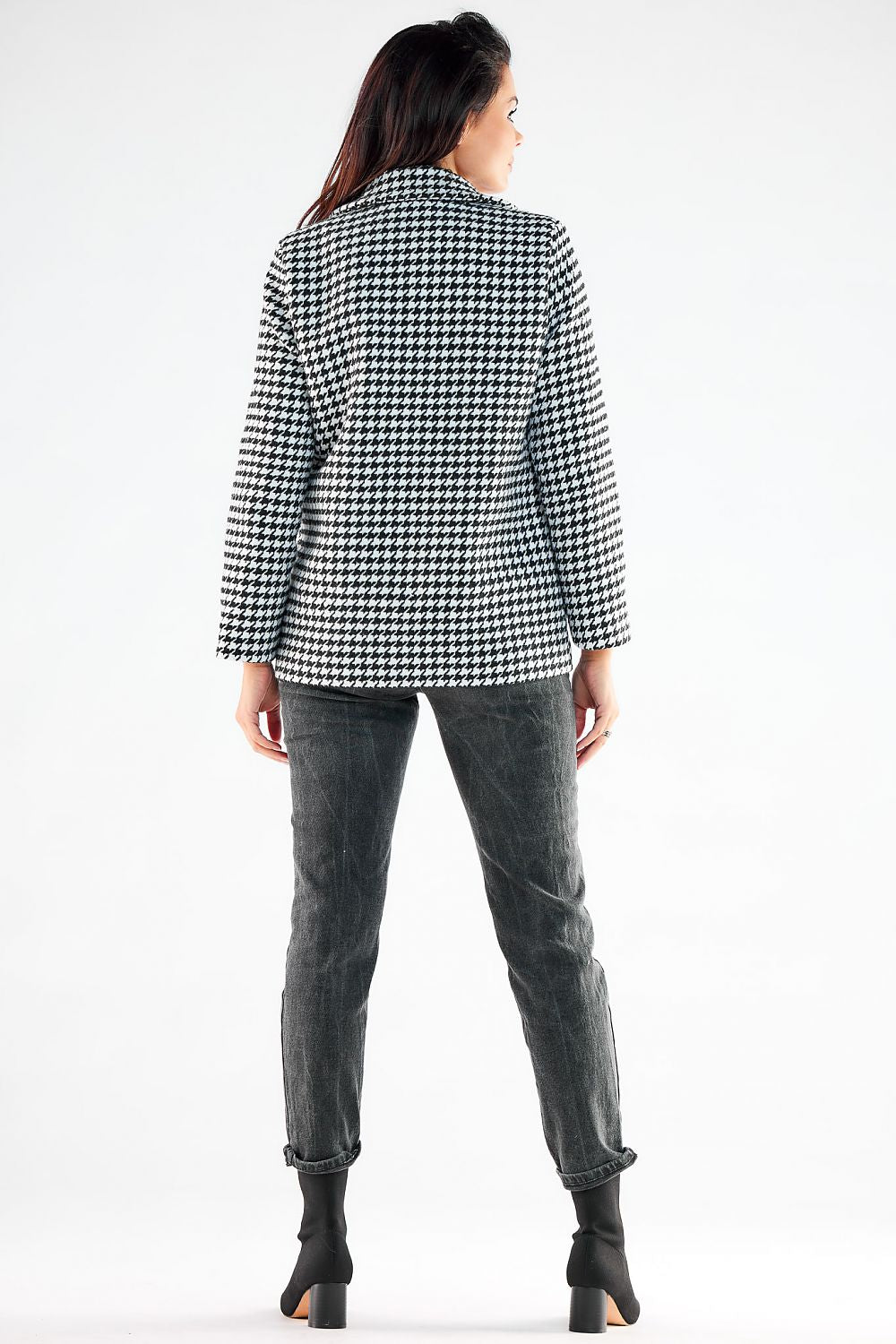 Elegant woman showcasing the back view of a stylish black and white houndstooth patterned jacket by Awama, elegantly paired with chic grey jeans.