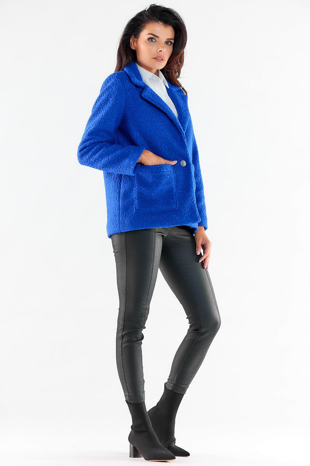 Chic side view of a woman wearing a bright blue jacket by Awama, complemented with sleek leather trousers for a refined look.