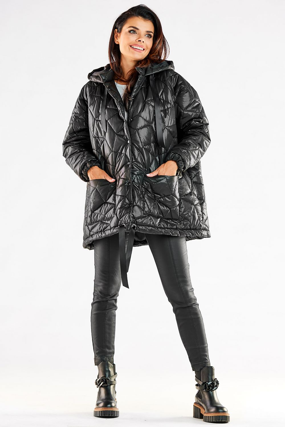 Fashionable model in a black oversized quilted jacket, featuring an adjustable hood and practical front pockets, exuding luxury and comfort for cold weather.