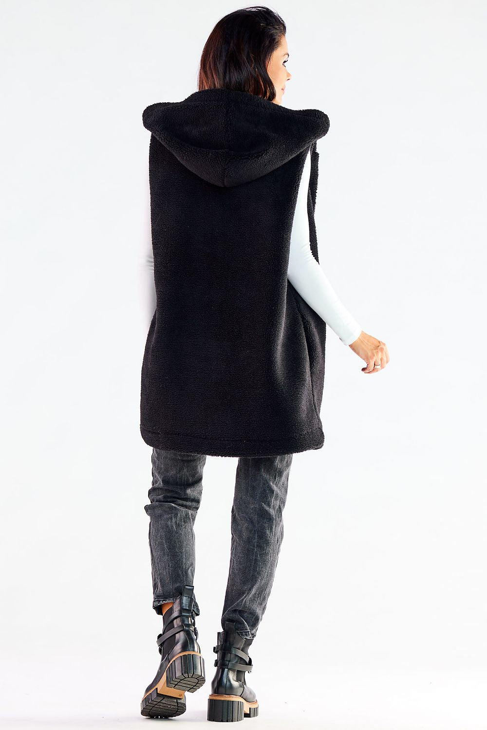 Elegant Awama hooded gilet vest in luxurious black fabric, showcasing a stylish silhouette with a hood. Perfect for layering, designed for comfort and warmth, ideal for cool weather. Styled with denim trousers and chic black boots, perfect for a sophisticated casual look.